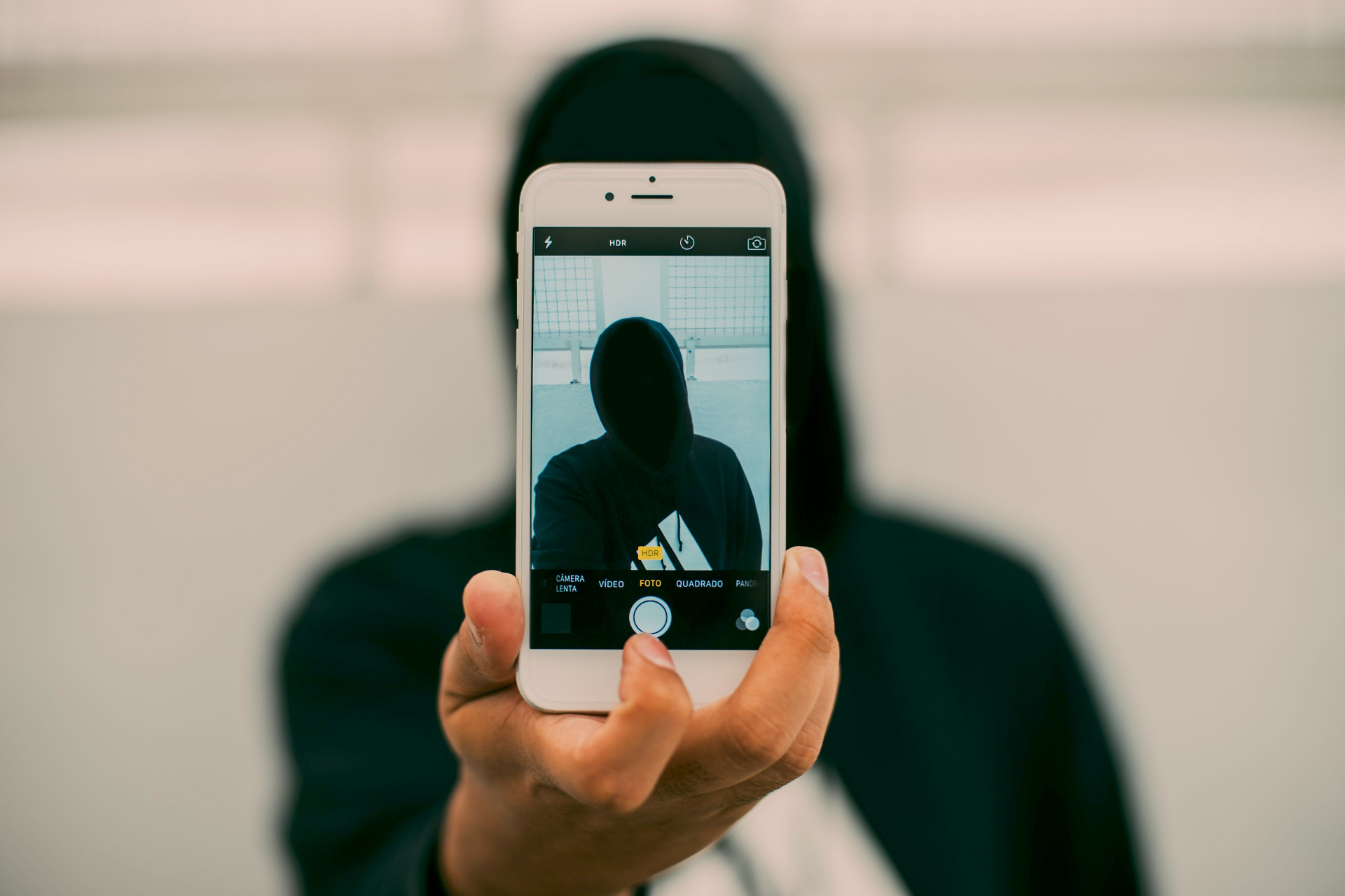 Persoon in capuchon houdt smartphone omhoog met camera-interface, symboliseert anoniem nepprofiel en identiteitsmisbruik online